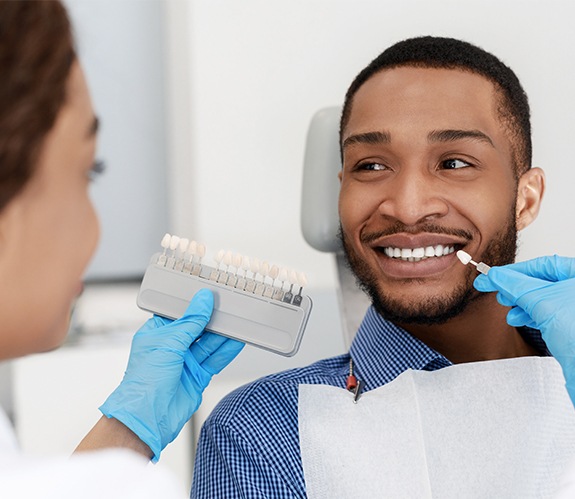 Man's smile compared with porcelain veneer shade chart during cosmetic dentistry exam