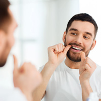 Younger male flossing his teeth at home 