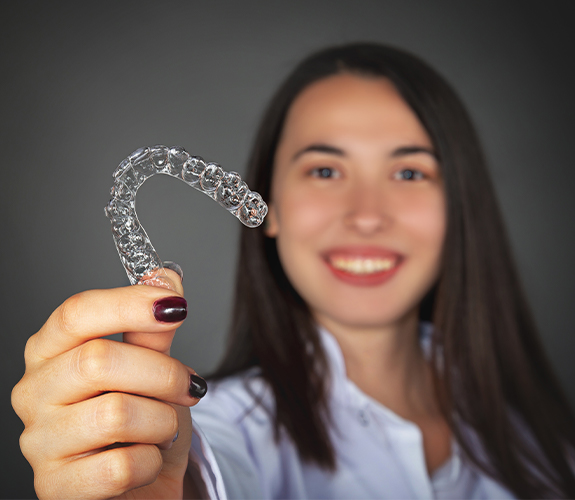 Smiling woman holding up her Invisalign tray