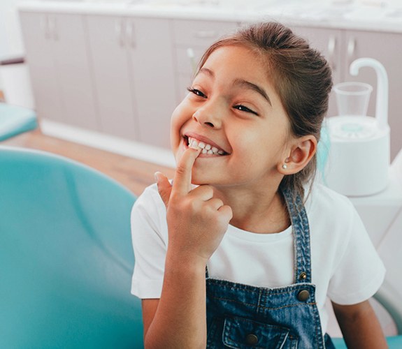 Girl smiling and pointing to teeth after Phase 1 orthodontics in Naperville, IL