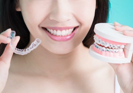 Woman holding an Invisalign tray and smile with traditional braces