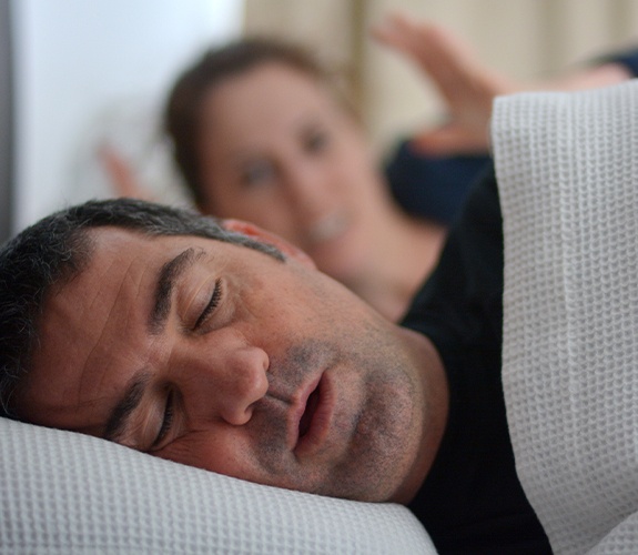 Frustrated woman in bed next to snoring man who needs sleep apnea treatment
