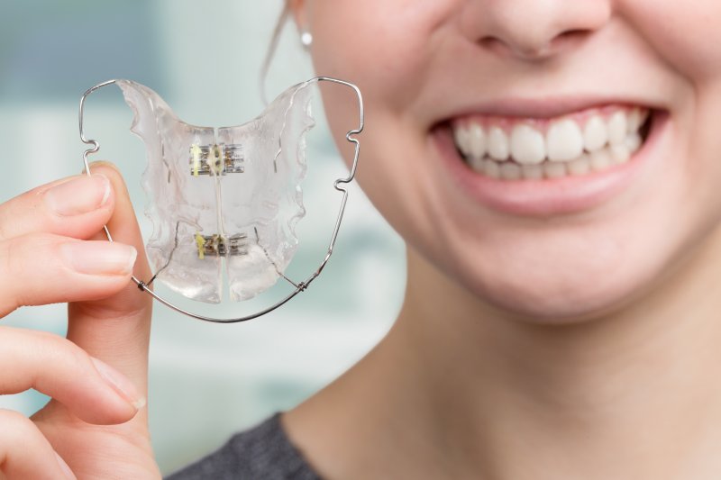 Smiling girl holding up an orthodontic retainer